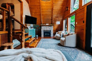 Ein gemütliches Blockhaus-Interieur mit Kamin aus Stein, einer Holztreppe und einer komfortablen Sitzecke.