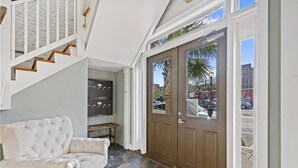 A foyer with a staircase, a door with a view of parked cars, and a seating area.