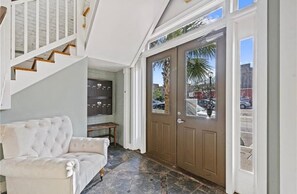 A foyer with a staircase, a door with a view of parked cars, and a seating area.
