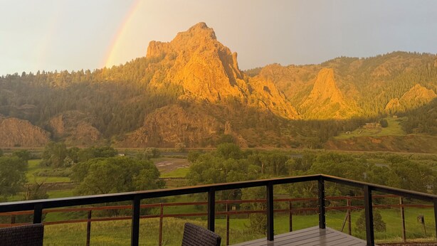 Een berglandschap met een regenboog, een houten terras en uitzicht op een vallei.
