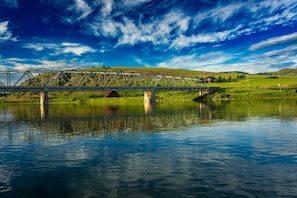 Un pont metàl·lic sobre un riu tranquil amb un cel serè.