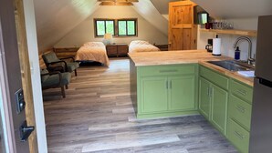 Een compacte, moderne loft slaapkamer met een kitchenette, houten balken en een groot raam.