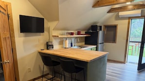 Een kleine keuken met een houten aanrecht, twee barkrukken, een koffiezetapparaat en een flatscreen televisie die aan de muur is bevestigd.