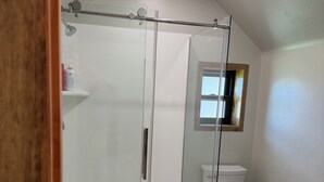 Een badkamer met een douchecabine van glas, een toilet en een houten vloer.