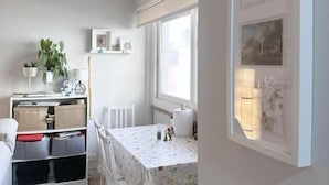 Cozinha compacta com armários brancos, mesa de jantar com cadeiras e janela que permite entrada de luz natural.