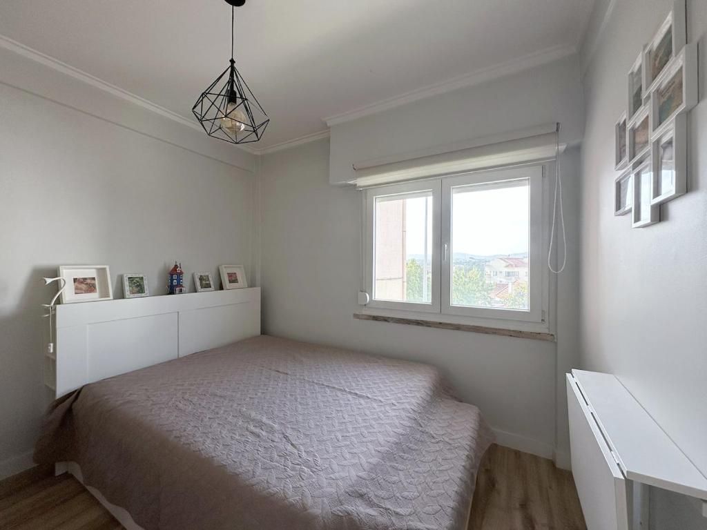 A bedroom with a bed, a window, and a wall-mounted shelf with framed pictures.