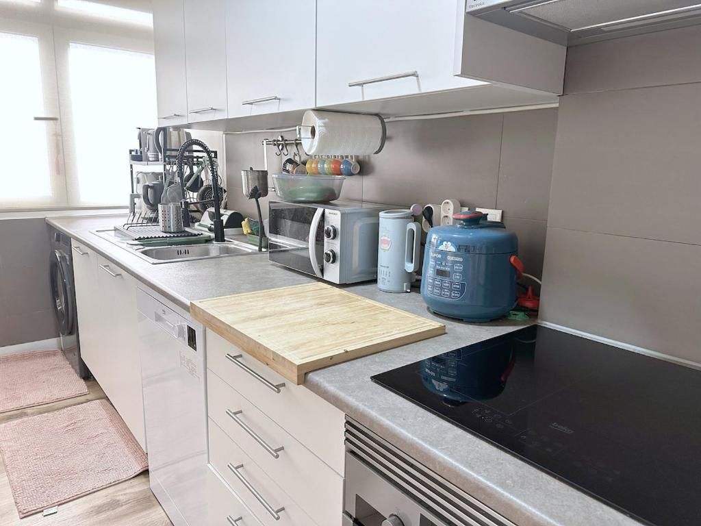 Eine moderne Küche mit weißen Schränken, einer schwarzen Induktionskochplatte, einem Toaster, einem Wasserkocher und einem Wasserspender.