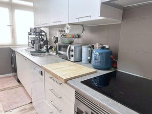 Una cocina moderna con armarios blancos, una placa de inducción negra, un tostador, un hervidor y un dispensador de agua.