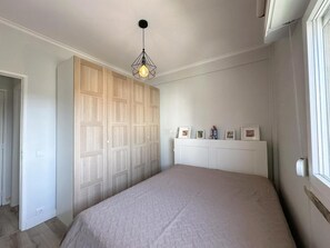 Ein Schlafzimmer mit einem Bett, einem Kleiderschrank, einer Pendelleuchte und einem Fenster.