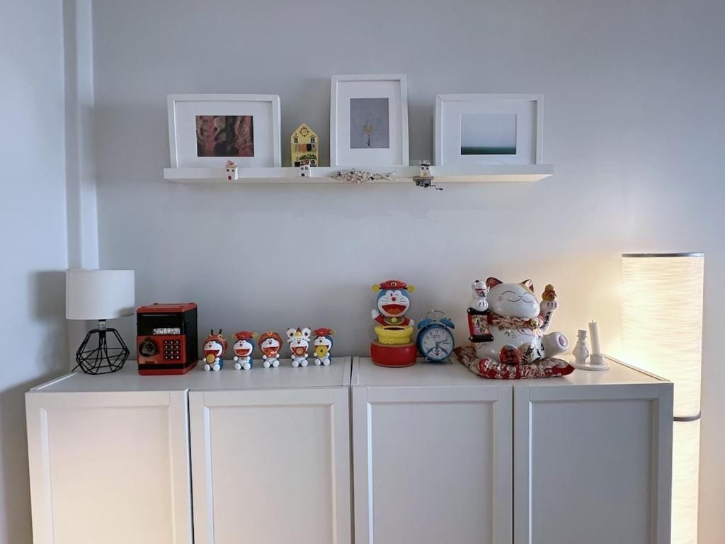 Un mueble blanco con un estante superior que contiene fotografías enmarcadas, un reloj y figuritas.
