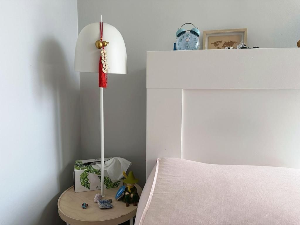 Ein Schlafzimmer mit einem Bett, einem Nachttisch mit Lampe, einer Uhr und einem kleinen Regal mit Dekoration.