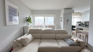 Uma sala de estar moderna com sofá seccional, área de jantar com mesa e cadeiras, e cozinha com armários e eletrodomésticos.