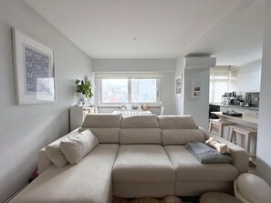 A modern living room with a sectional sofa, a dining area with a table and chairs, and a kitchen area with cabinets and appliances. - Casa Emon With Moomin Near Beach 2 Bedroom (Cascais)