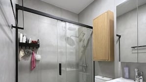 Casa de banho moderna com cabine de duche em vidro, sanita e toucador com armários.