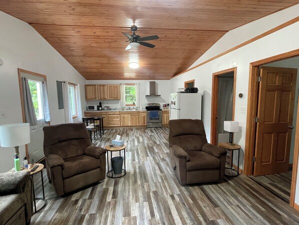 A spacious living area with two brown armchairs, a small round table, and a ceiling fan.