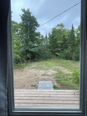 A view through a window of a wooden deck leading to a grassy area with trees.