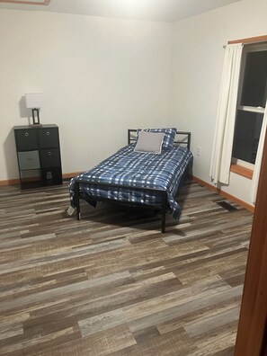 A bedroom with a bed, a nightstand, a lamp, and a window.