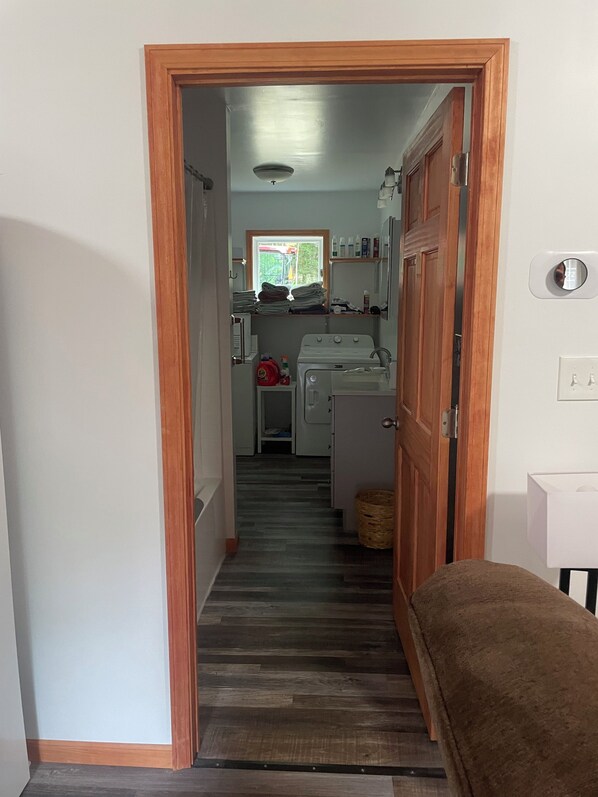 A narrow hallway leading to a laundry area with a washing machine, a dryer, and stacked laundry.