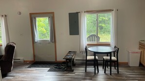 Una habitación con piso de madera, una mesa de comedor con sillas, un banco, una puerta y ventanas con cortinas.