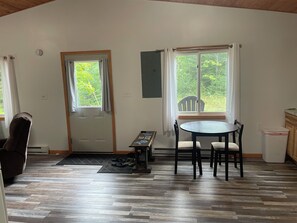 A room with a wooden floor, a dining table with chairs, a bench, a door, and windows with curtains.