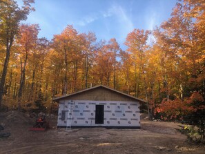 A small wooden cabin with a metal roof, surrounded by a forest with autumn-colored leaves.