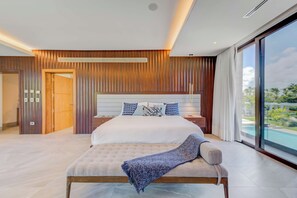 A modern bedroom with a large bed, a wooden panel wall, and a view of a swimming pool. - Beachfront Cap Cana Estate · Private Beach · Spa (Punta Cana)