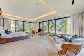 A modern hotel room with a large bed, a sofa, a TV, and a view of palm trees. - Beachfront Cap Cana Estate · Private Beach · Spa (Punta Cana)