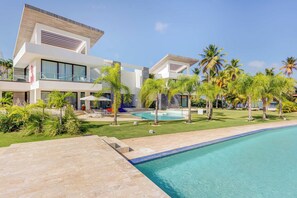 A modern two-story hotel with a swimming pool, palm trees, and a clear blue sky. - Beachfront Cap Cana Estate · Private Beach · Spa (Punta Cana)