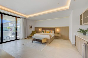 A modern bedroom with a large bed, a sliding glass door to a balcony, a small seating area, and a nightstand. - Beachfront Cap Cana Estate · Private Beach · Spa (Punta Cana)