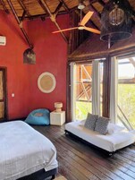 Habitación con dos camas, ventilador de techo, ventana con vistas y una lámpara de fibras naturales.