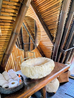 Habitación con techo de bambú, un lavabo de piedra y una cesta con toallas y artículos de aseo.