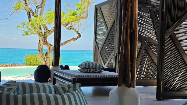 A beachside lounge with a view of the ocean, a tree, and a patterned wall. - ENAI DEL MAR (Bolívar)