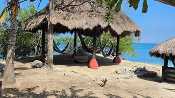 Escena de playa con cabañas de techo de paja, palmeras y cielo azul despejado.