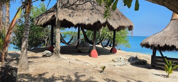 Escena de playa con cabañas de techo de paja, palmeras y cielo azul despejado.