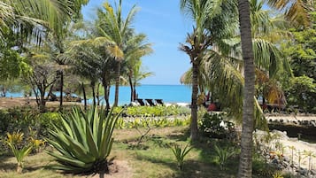 A tropical garden with palm trees, a beach, and lounge chairs.