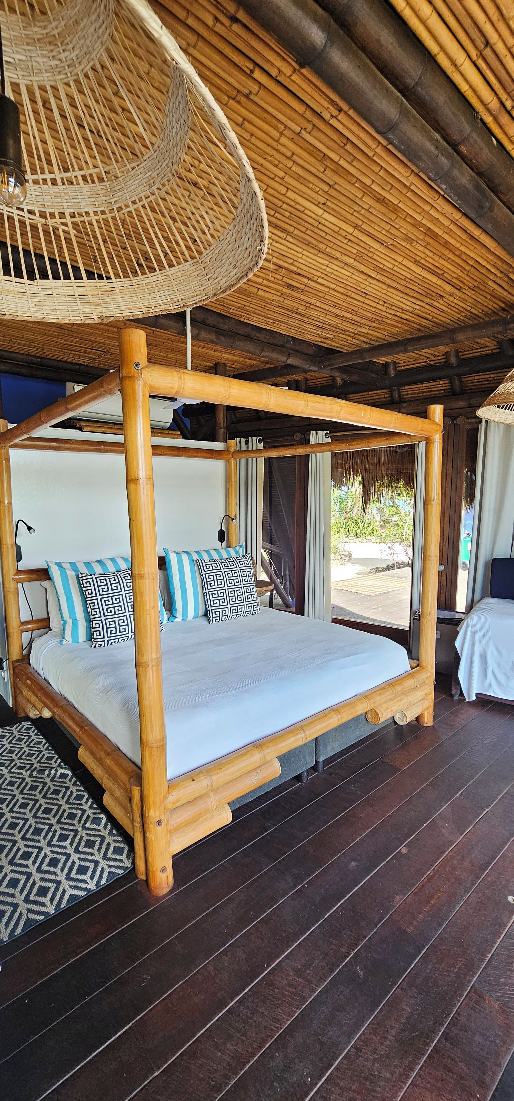 A bed with a wooden frame and a woven headboard, a patterned rug, and a large woven ceiling fan.