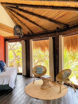 A room with a bed, two wicker chairs, a woven rug, and a ceiling with a bamboo-like pattern.