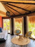 Una habitación con una cama, dos sillones de mimbre, un tapete tejido y un techo con diseño similar al bambú.