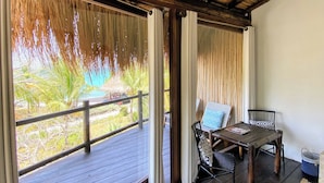 A covered outdoor area with a wooden deck, a table with chairs, and a view of greenery. - ENAI DEL MAR (Bolívar)