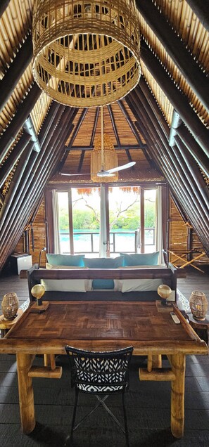 Quarto de sótão com mesa de madeira, uma cadeira e uma janela grande com vista para vegetação.
