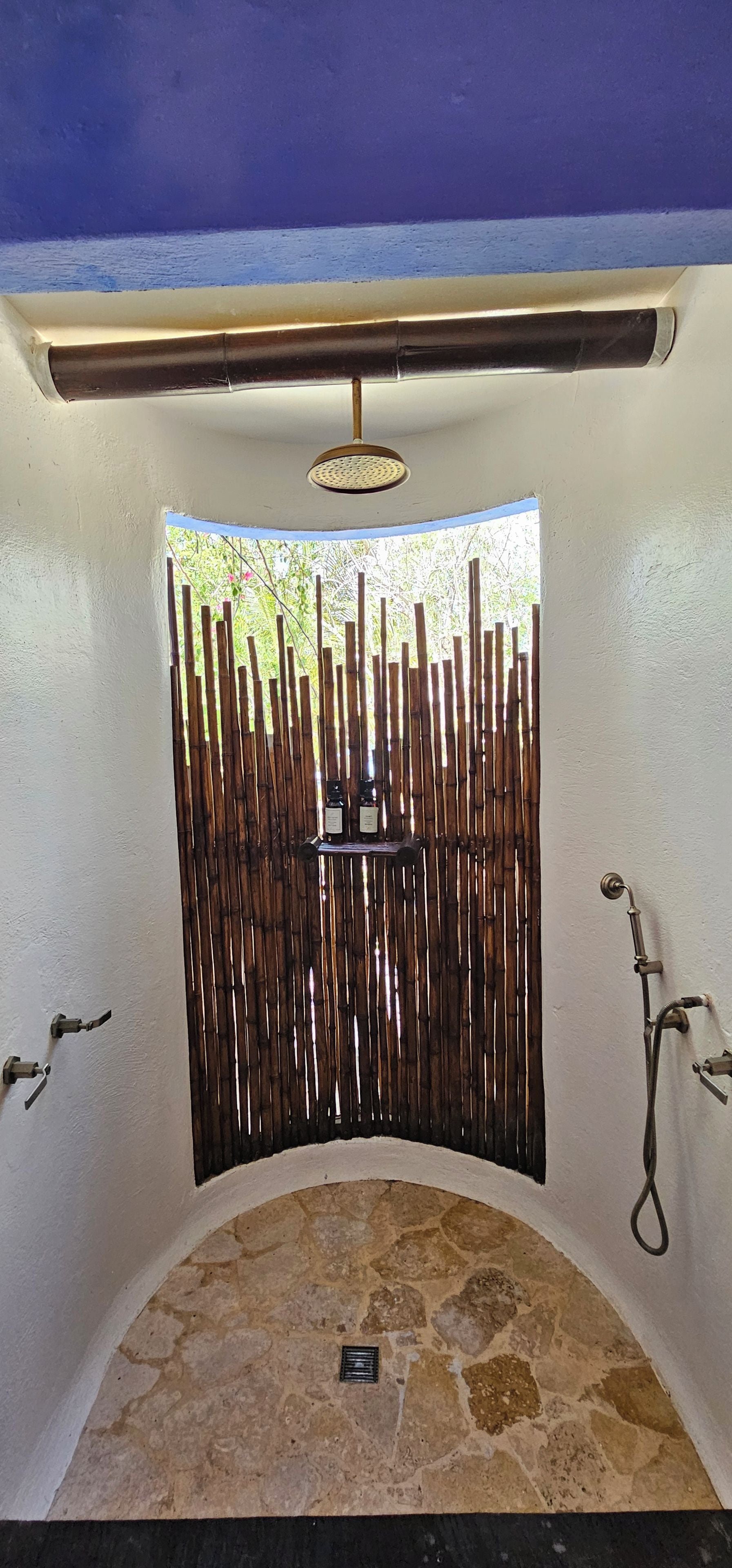 A stone-tiled shower area with a bamboo privacy screen, a metal shower head, and a faucet.