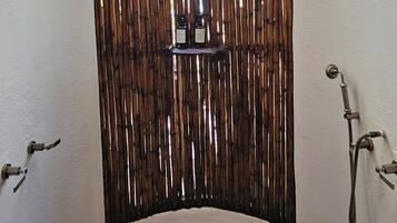 A stone-tiled shower area with a bamboo privacy screen, a metal shower head, and a faucet.