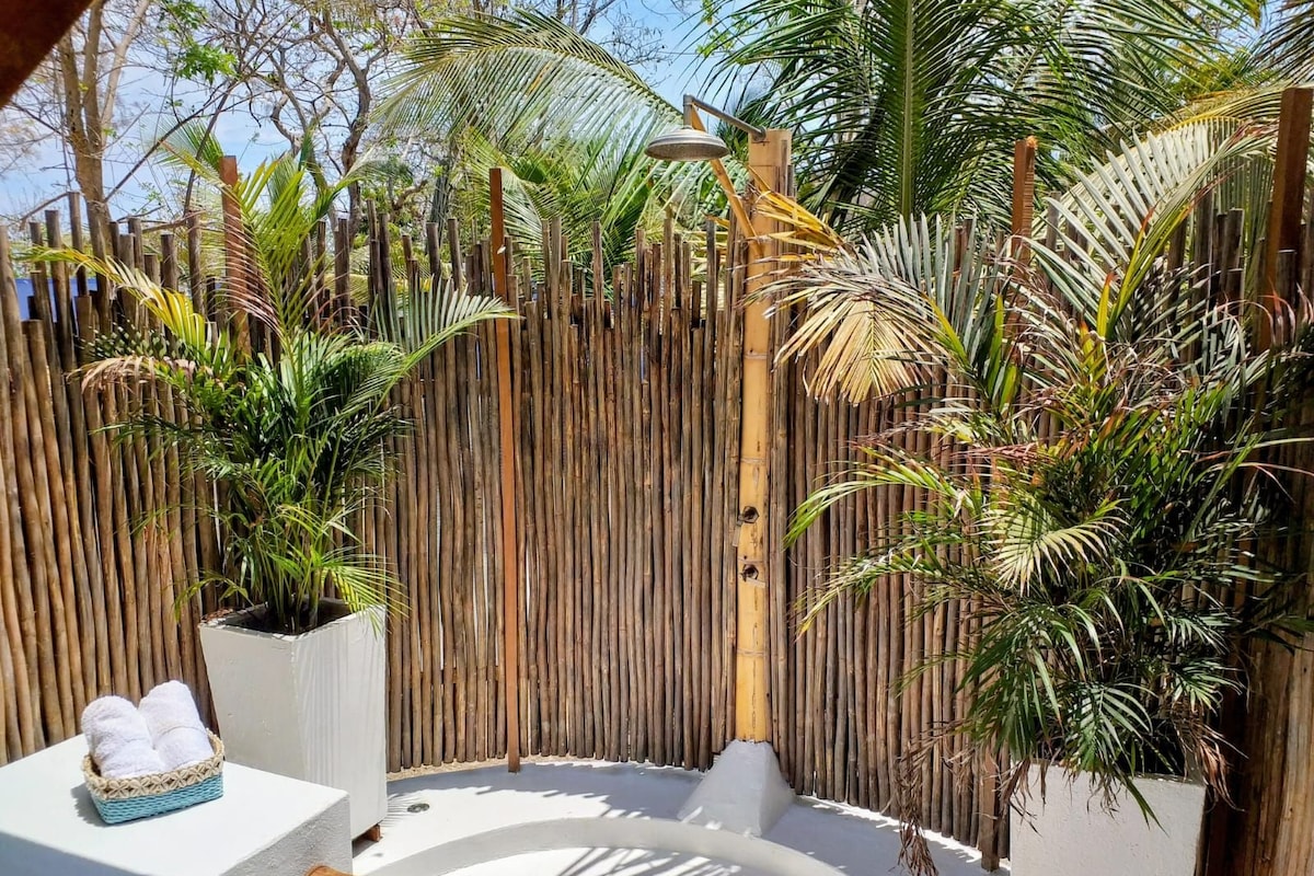 A circular outdoor area with a bamboo fence, potted plants, and a white structure with towels.