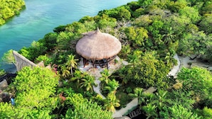 A thatched-roof structure surrounded by lush greenery and a clear blue water body. - ENAI DEL MAR (Bolívar)