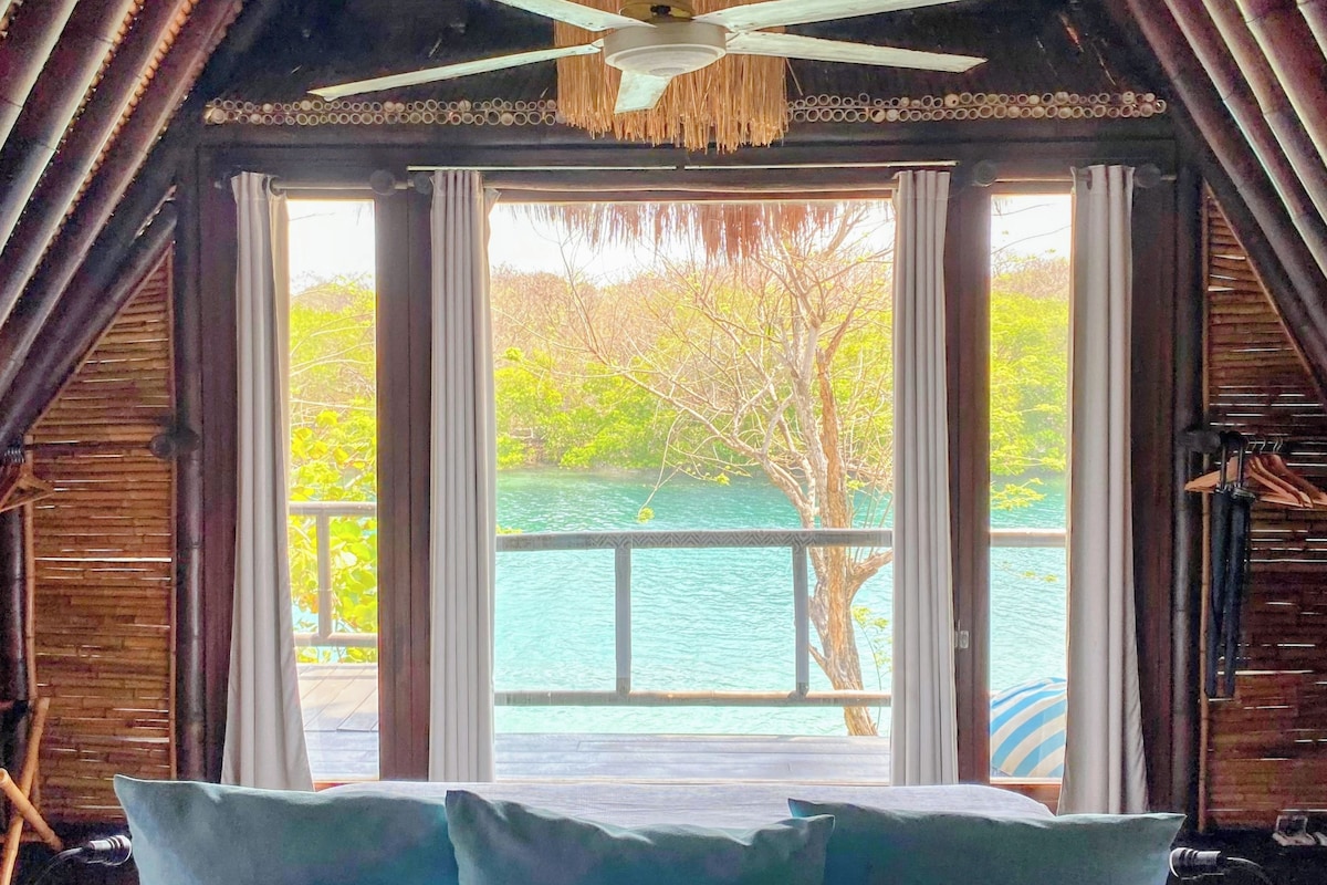 A room with a bed, a ceiling fan, and a view of a body of water.