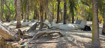 Escena de playa con asientos blancos acolchados y un tronco grande al frente.