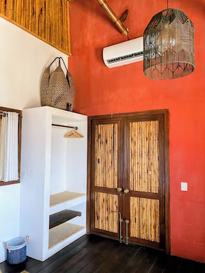 A room with a red wall, a white cabinet, a hanging basket, a door with a bamboo design, and a hanging light fixture.