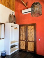 Una habitación con una pared roja, un armario blanco, una cesta colgante, una puerta con diseño de bambú y una lámpara colgante.