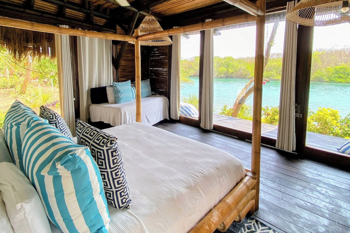 A room with a bed, a ceiling fan, and a view of the sea.