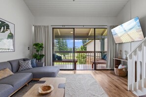 A modern living room with a grey sofa, a wooden coffee table, and a flat-screen TV mounted on the wall.